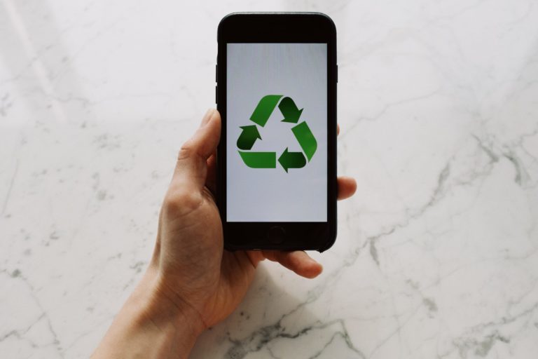 From above view of faceless person holding mobile phone with white screen and green recycle logo above marble surface