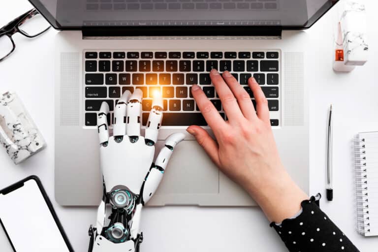 a person typing on a laptop with a robotic hand next to it