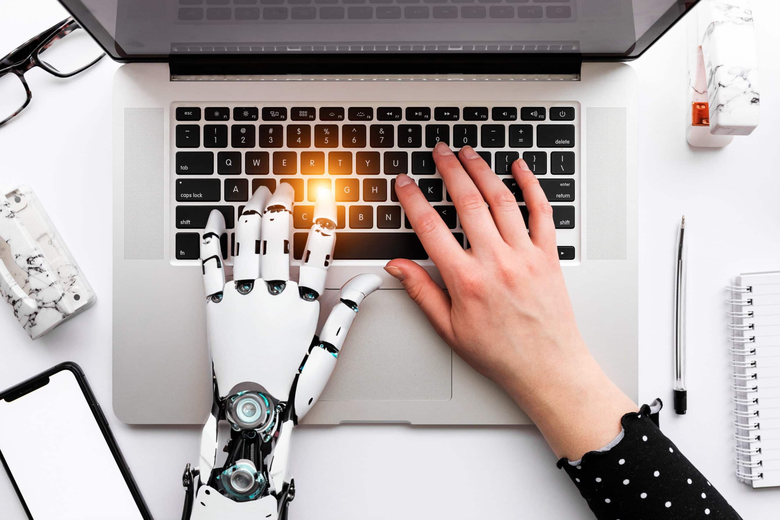 a person typing on a laptop with a robotic hand next to it