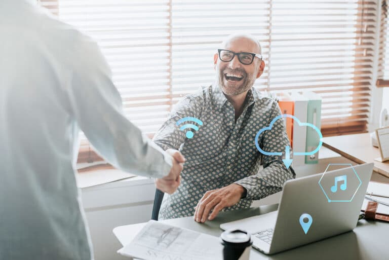 two men shaking hands in front of a laptop