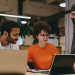 a group of people sitting around a table with laptops